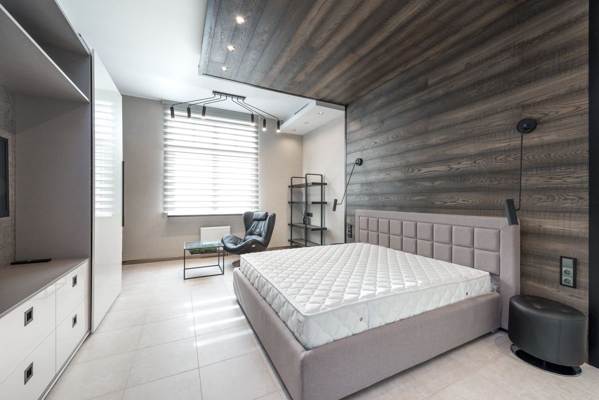 Bare mattress on a bed frame beside a shuttered window