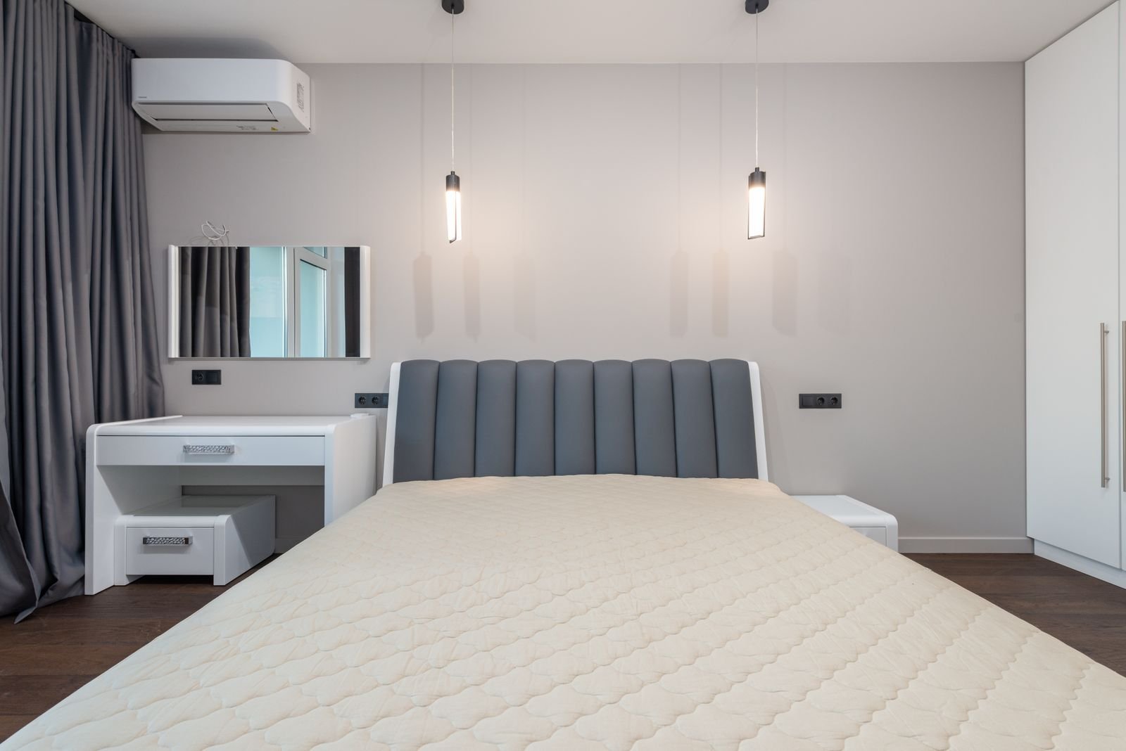 Bed with a grey upholstered headboard next to a white dressing table