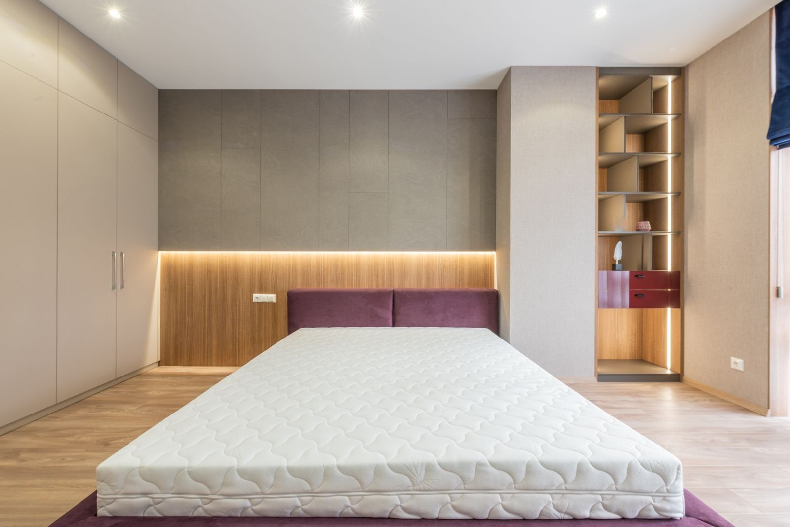 Bedroom with a bare mattress, upholstered headboard and built-in shelving
