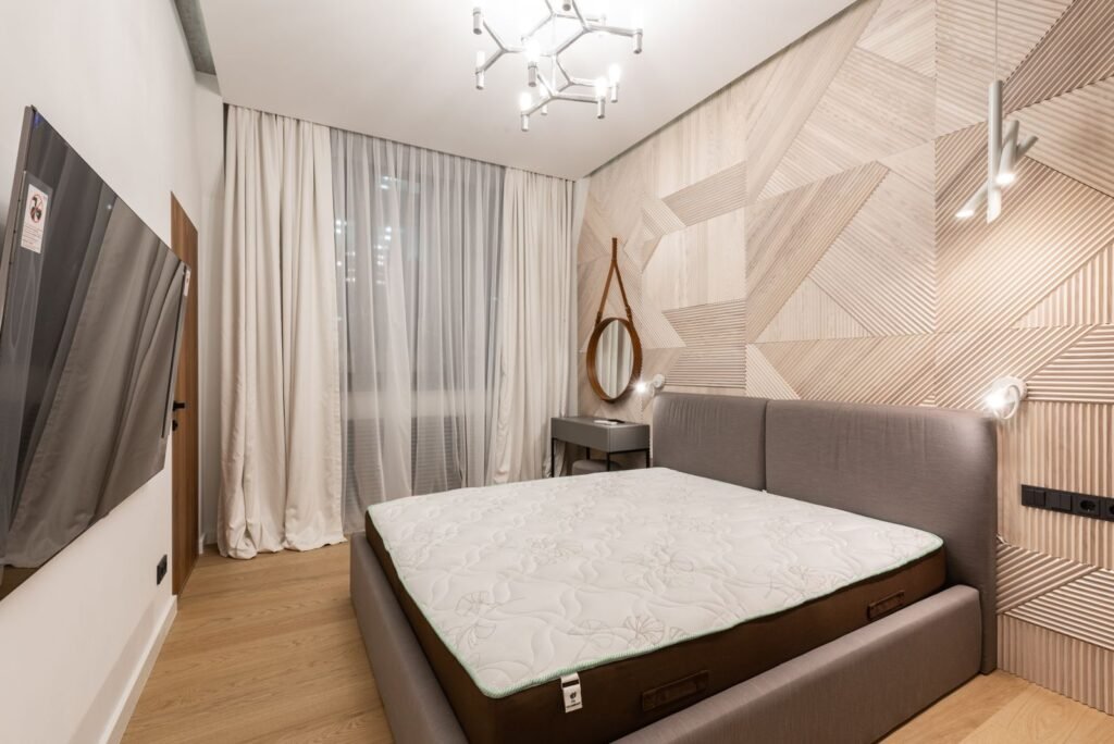 Bare mattress on a bed beside floor-length curtains in an airy bedroom