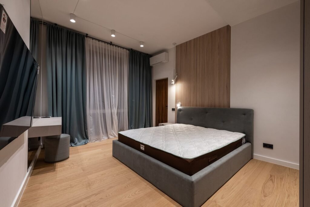 Bed with an upholstered headboard and bare mattress beside heavy curtains