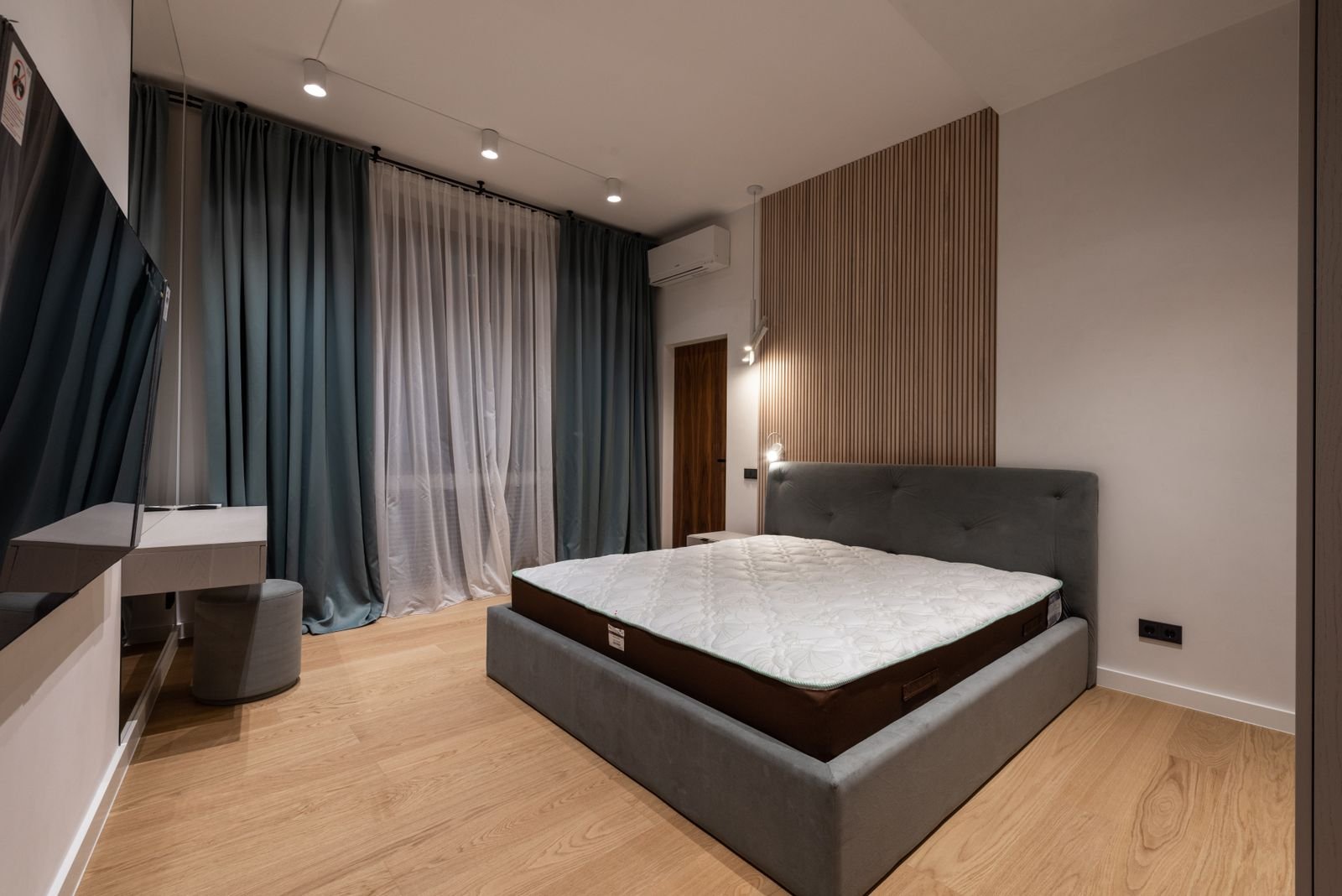 Bed with an upholstered headboard and bare mattress beside heavy curtains