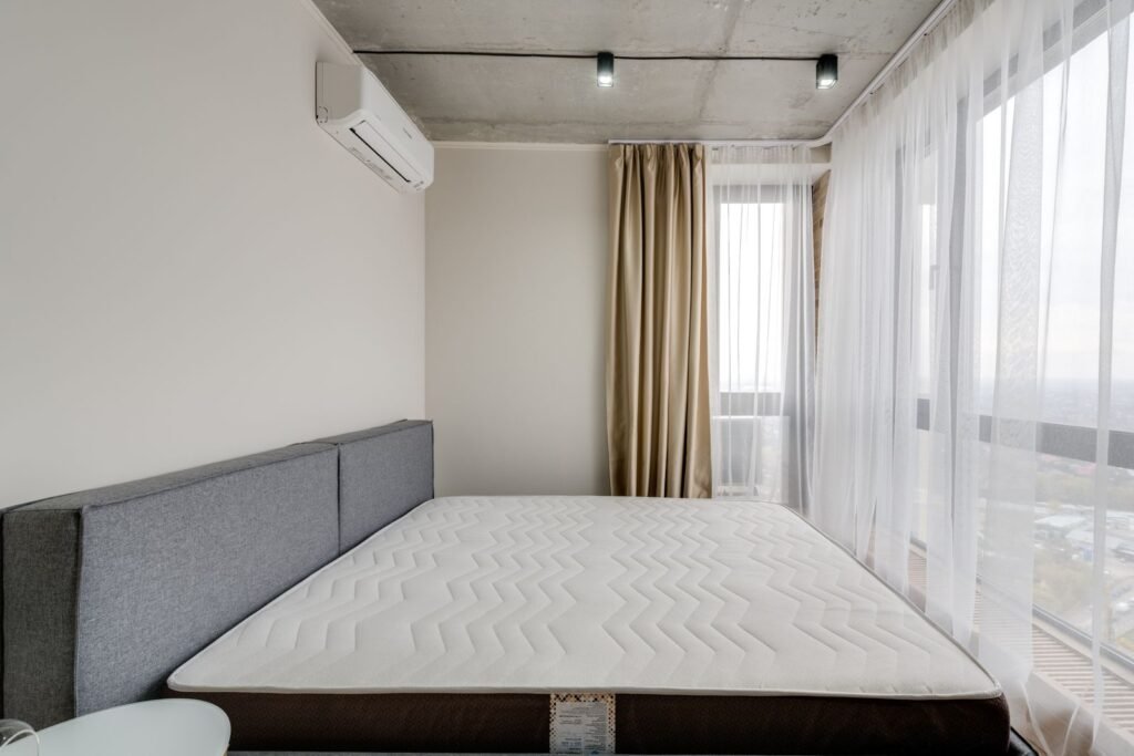 Bare mattress on a low bed frame in a plain bedroom with floor-length curtains