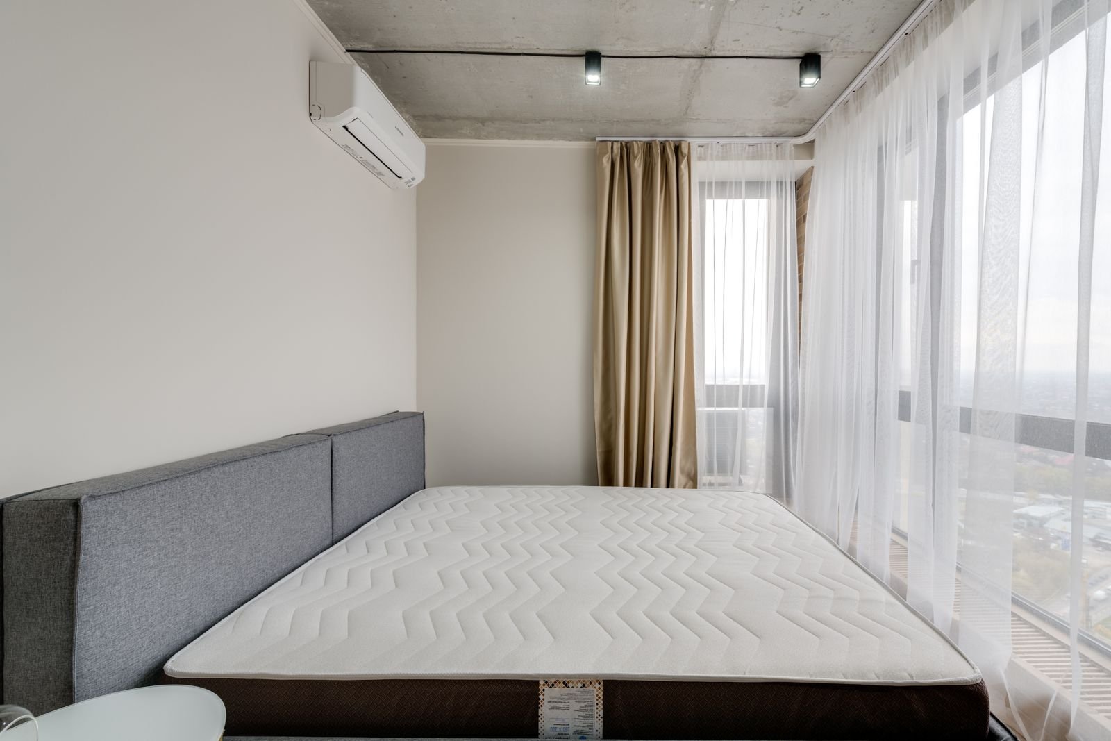 Bare mattress on a low bed frame in a plain bedroom with floor-length curtains