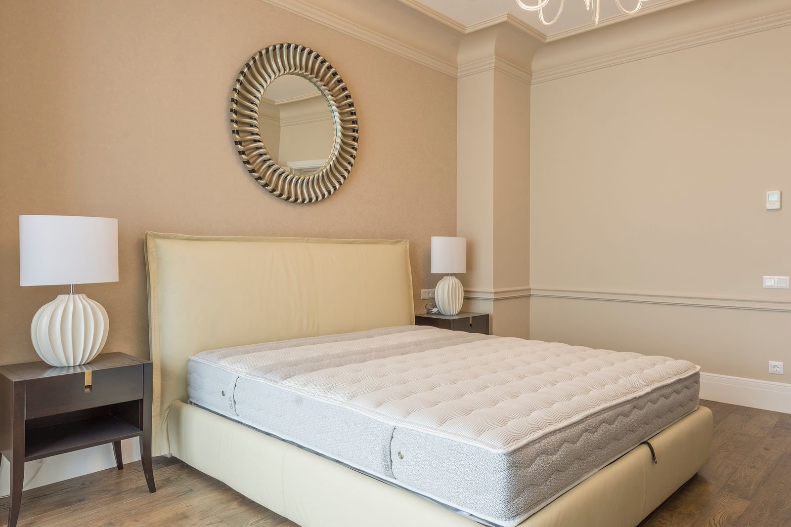 Bare mattress on a bed with a cream headboard and matching bedside lamps