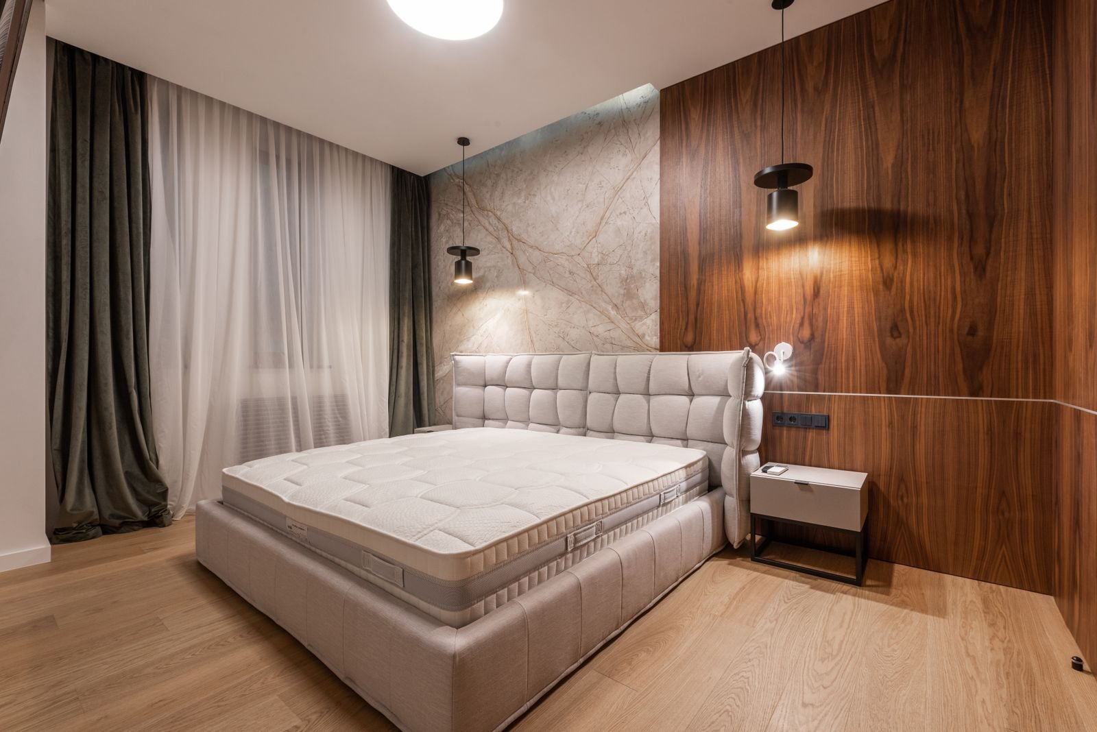 Bare mattress on a bed with a deep quilted headboard and warm lighting