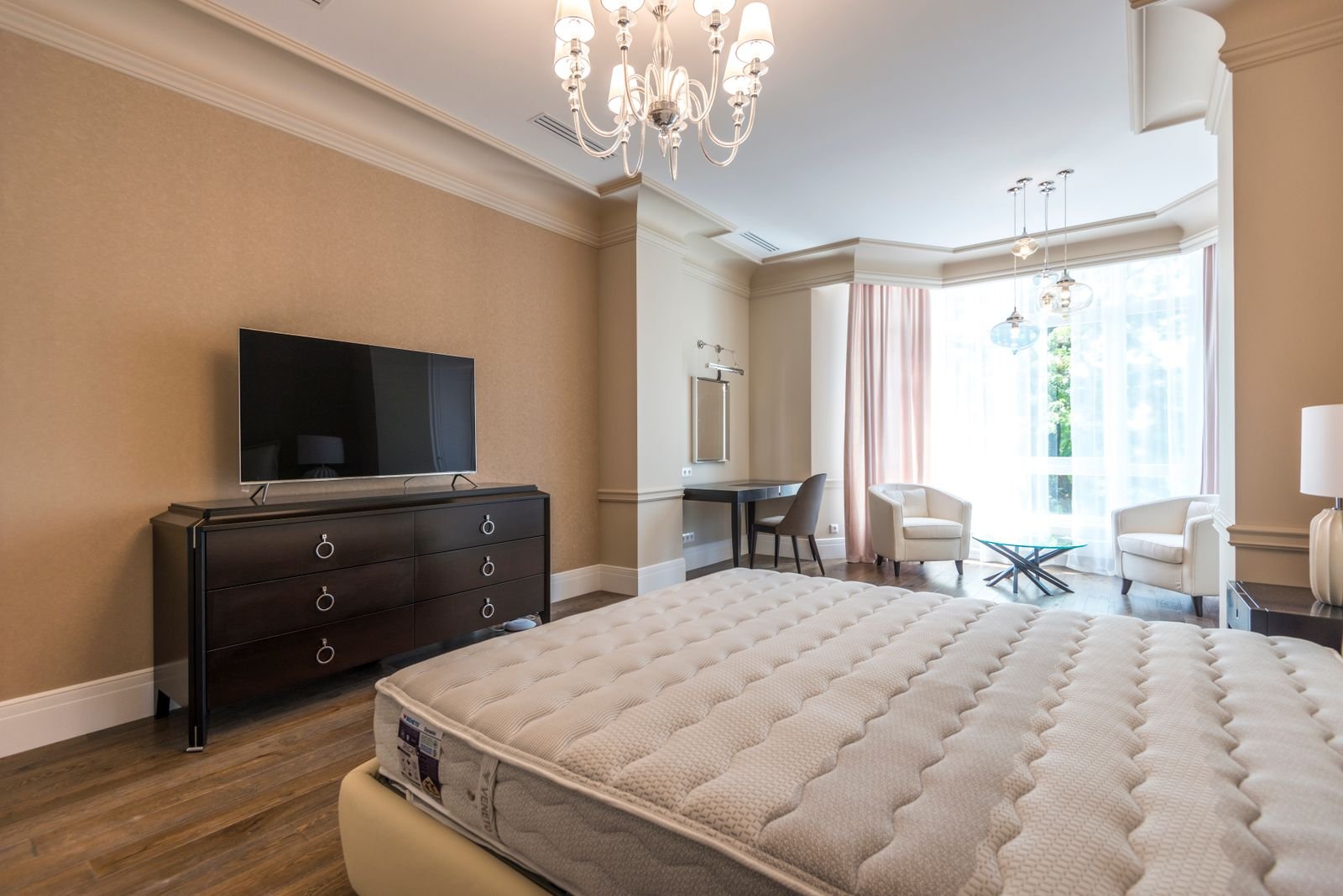 Furnished rental bedroom with a bed, wall-mounted television and a seating area by the window