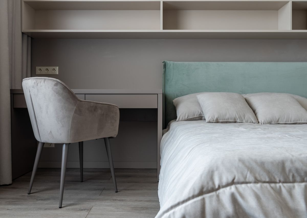 Bedroom with a teal upholstered headboard, white bedding and a grey armchair