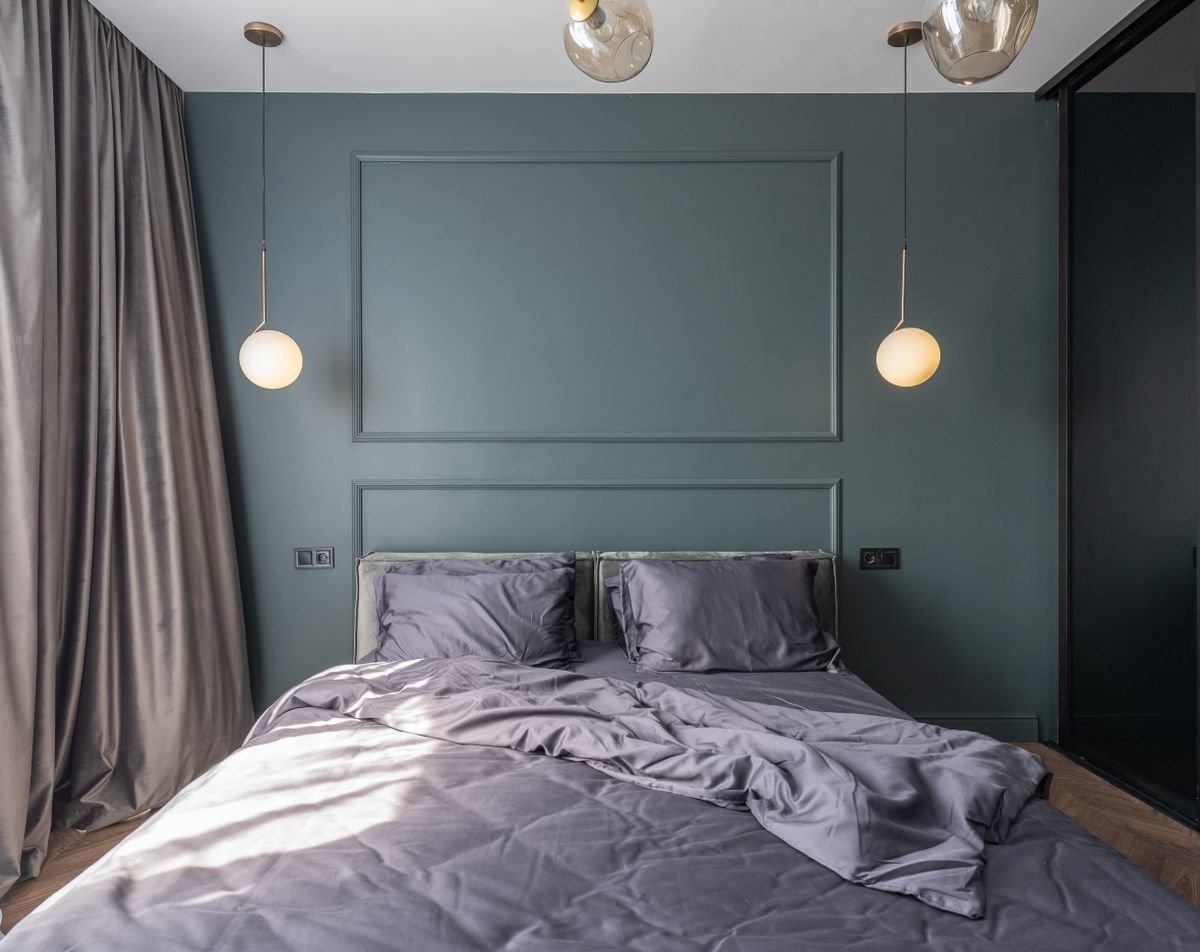 Bedroom with a dark teal panelled wall, grey bedding and hanging pendant lights