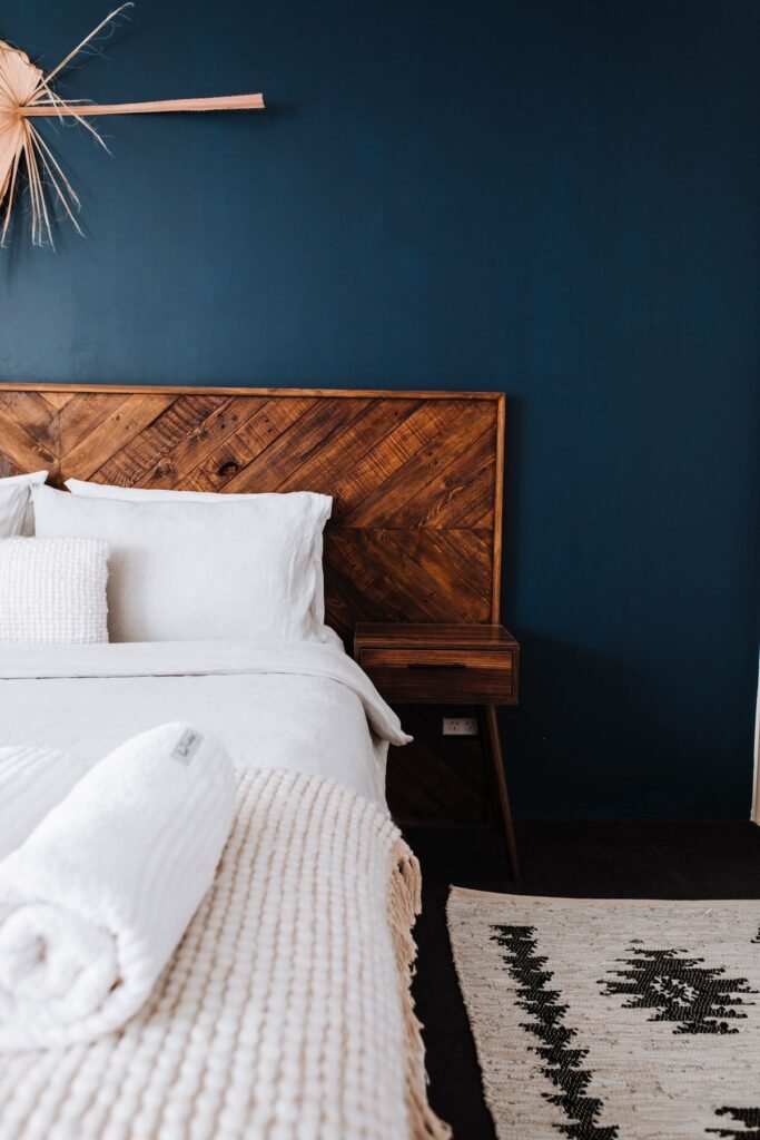 White bedding and pillows against a dark wooden headboard and a navy wall