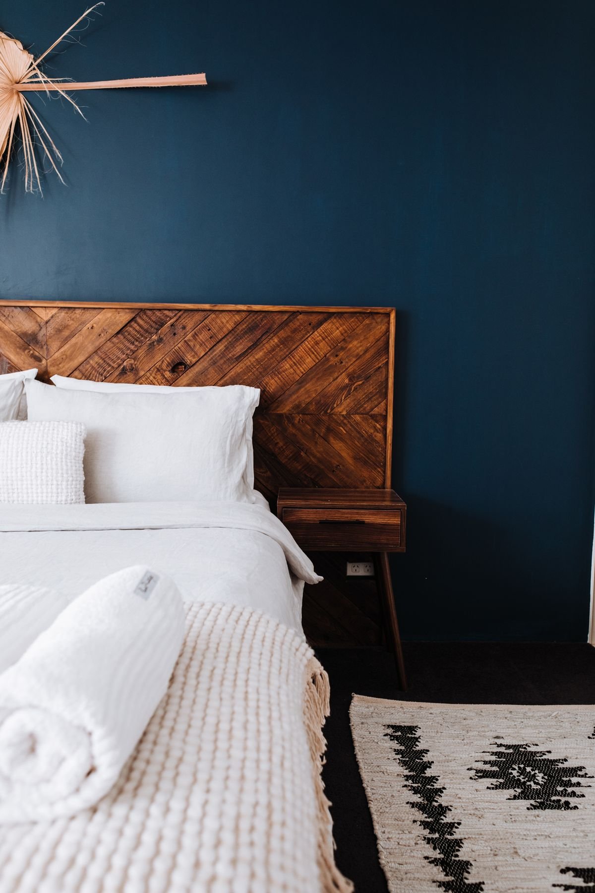 White bedding and pillows against a dark wooden headboard and a navy wall