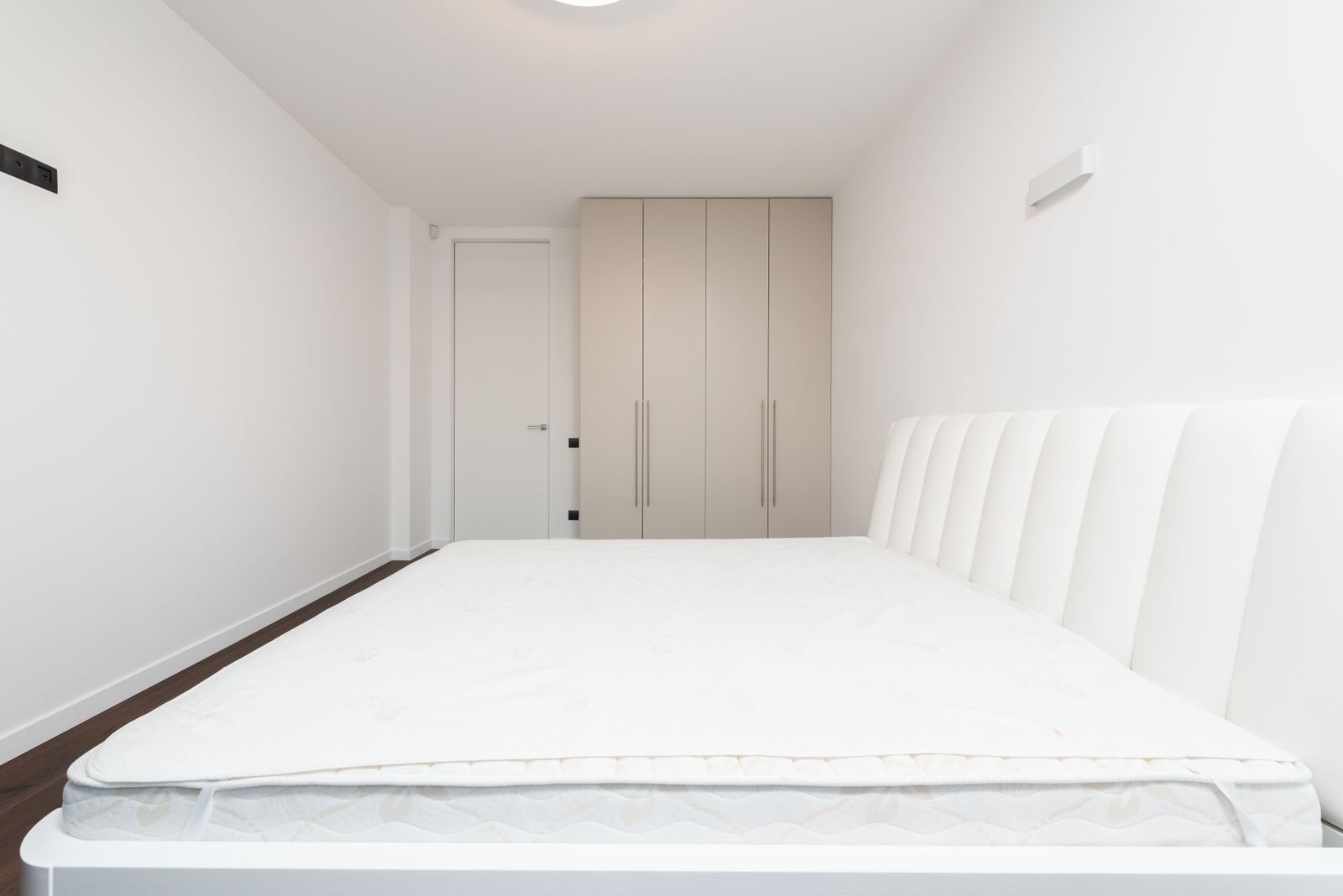Bright white bedroom with a bare mattress and fitted wardrobes