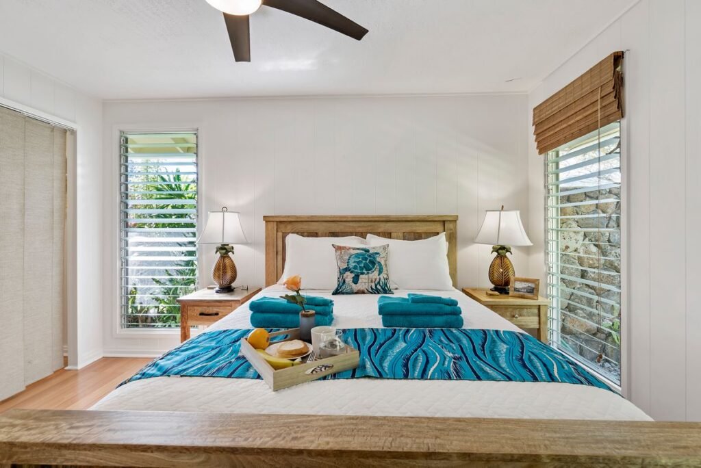 Wooden bed with a teal throw in a bright bedroom with plantation shutters