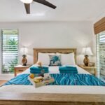 Wooden bed with a teal throw in a bright bedroom with plantation shutters